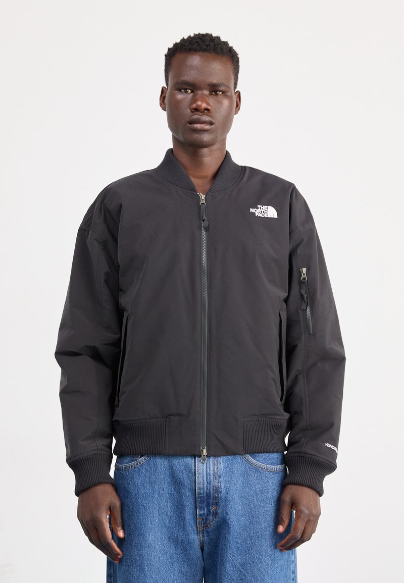 Giacca bomber nera con zip frontale, polsini e fondo a costine, logo sul petto, tasche laterali e tessuto testurizzato. Design leggero e aderente.