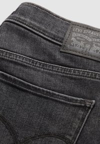 Jeans de denim gris oscuro con una textura sutil, que presentan un parche de cuero en la parte trasera con un logo grabado y costuras clásicas a lo largo de las costuras.