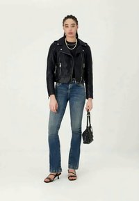 Black leather motorcycle jacket with zippered pockets, paired with fitted blue jeans, black strappy heels, and a small black handbag.