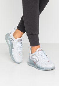 Vita sportskor i vitt med mesh-överdel, vadderad tunga och röda detaljer. Genomskinlig luftkuddar-sula, rund tådesign och texturerad detalj.