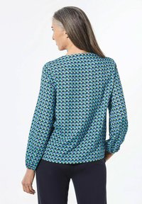 Blusa blu con motivo geometrico a triangoli in verde e blu marine, maniche lunghe con polsini elasticizzati e vestibilità rilassata.