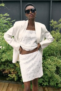 Set di top corto e gonna con texture floreale bianca, design stratificato con silhouette aderente, abbinato a un blazer oversize di colore chiaro. Occhiali da sole neri.