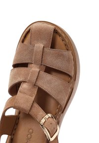 Sandalo in suede marrone con cinturini incrociati, una soletta in pelle liscia e una suola piatta e testurizzata con una fibbia in oro.