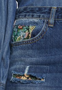 Calças de ganga com a barra desgastada e detalhe em bordado floral no bolso. Tom azul com costuras amarelas e tecido texturizado.