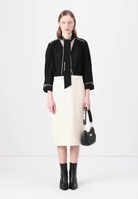 Črna bluza z dolgimi rokavi in belimi detajli, slišna oblačila z navezanim ovratnikom, v kombinaciji s prilegajočo kremno svilenko, črnimi gležnjarji in prešito torbico.