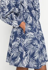Robe navy avec motif de feuilles blanches, dotée de manches longues et d'une taille élastique. Comprend des poches latérales et une coupe décontractée. Tissu en coton lisse.
