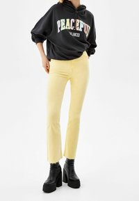 Czarna bluza z kapturem z napisem "PEACEFUL", zestawiona z jasnopomarańczowymi rozszerzanymi dżinsami z postrzępionymi nogawkami oraz czarnymi botkami na platformie.