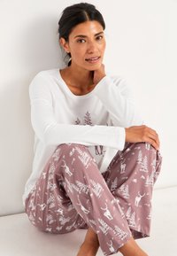 Vit långärmad topp med trädgrafik; mauve pyjamasbyxor med vita mönster av djur och träd; mjukt tyg, avslappnad passform och medelhög midja.