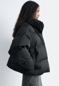 Black puffer jacket with a high collar, featuring a quilted design and a boxy shape. Smooth texture, oversized fit, and no visible hardware.