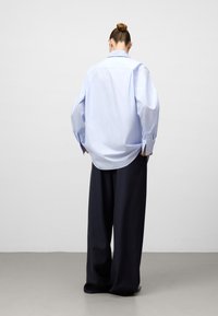 Jasnoniebieska, oversize koszula z guzikami, z długim rękawem i zaokrąglonym dołem, w połączeniu z luźno dopasowanymi, ciemnoniebieskimi spodniami. Gładka tekstura materiału.