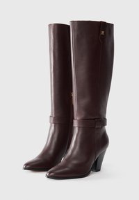 Stivali in pelle bordeaux alti fino al ginocchio, con punta affusolata, silhouette aderente, fascia decorativa e design con tacco medio. Presentano un dettaglio con logo dorato.