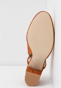 Sandale plate en daim beige avec semelle texturée beige et bride de cheville réglable, vue par le dessous sur fond blanc.