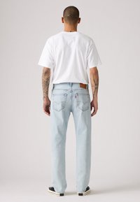 Jeans dritti blu chiaro con una toppa in pelle sul retro, texture in denim e due tasche posteriori, abbinati a una maglietta bianca semplice.