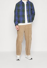 Rutiga skjortor i blått och grönt med gula accenter, tillsammans med beige kordbyxor och vita sneakers. Har framfickor och knappar.