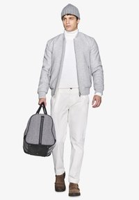 Grå bomberjakke, hvid turtleneck, beige bukser, brune sko. Bærer en duffelbag i sort og grå hørførelse med sorte accenter.