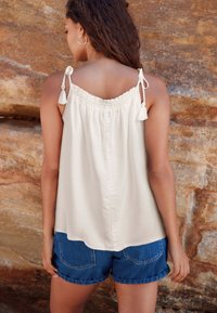 Light beige sleeveless top with gathered neckline and tie straps, paired with denim shorts featuring rolled cuffs and back pockets.