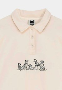 Camiseta tipo polo color crema pálido con una tapeta de tres botones que presenta un gráfico negro de seis perros dálmatas impresos en el centro.