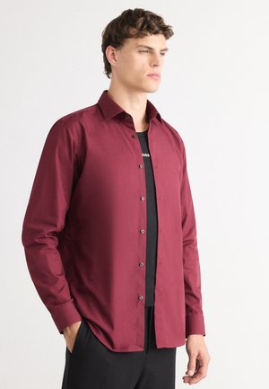Burgundy long-sleeve shirt with a button-up front, black buttons, and a spread collar worn over a black t-shirt. Made of smooth fabric.