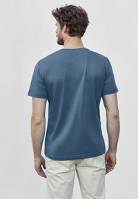 Modrá bavlněná tričko s kulatým výstřihem, krátkými rukávy a uvolněným střihem, zobrazené ze zadní strany na světlém pozadí.