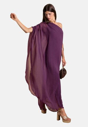 Vestido de gasa púrpura con un diseño asimétrico y mangas fluidas. Combinado con tacones de plataforma beige y un bolso pequeño marrón.