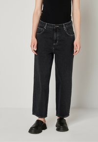 Zwarte denim wijde jeans met contrasterende stiksels, vijf zakken en een knoopsluiting, gecombineerd met zwarte instapschoenen.