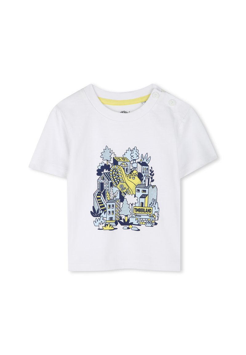 Camiseta de algodón blanca con un diseño gráfico azul y amarillo de una bota entre edificios y árboles ilustrados. Cierres de botón a presión en el hombro.