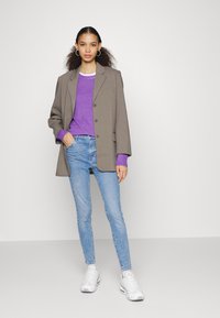 Blazer cinza oversized, suéter roxo, jeans skinny azul claro e ténis brancos. Tecido suave, ajuste elegante e detalhe minimalista em metal.