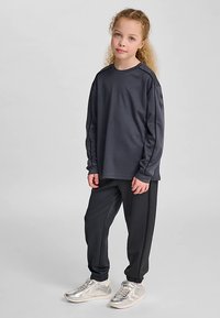 Mörkgrå långärmad tröja med rund halsringning, kombinerad med matchande avsmalnande byxor. Outfiten har ett mjukt tyg och en avslappnad passform. Silverfärgade sneakers.