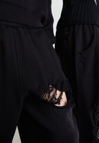 Sorte sweatpants med slidte detaljer, der har store huller med frynset kant. Blødt stof med en afslappet pasform, som er parret med en ribbet sort top.