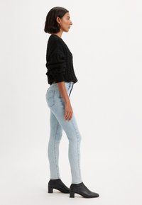 Fekete kötött pulóver, világoskék, enyhén használt skinny farmernadrág és fekete bokacsizma. A pulóver vastag ujjak és bordás mandzsetta jellemzi.