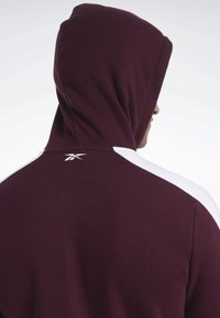 Felpa bordeaux con un accento bianco sulle spalle, dotata di cappuccio e di un piccolo logo sul retro. Realizzata in un tessuto morbido e strutturato.
