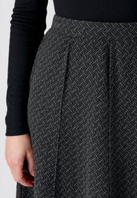 Zwarte rok met een gestructureerd visgraatontwerp, voorzien van plooien en een aansluitende tailleband, gecombineerd met een zwarte longsleeve top met ribbels.