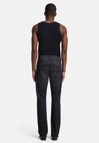 Zwarte geribbelde tanktop met een donkere spijkerbroek met rechte pijpen. Beschikt over twee achterzakken en een subtiele stikselpatroon. Schone uitstraling.