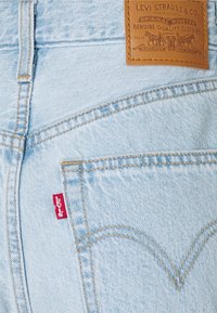 Ljusblå denimjeans med en läderlogotyp, kontrasterande sömmar, arcuate-design på bakfickan och en röd etikett.