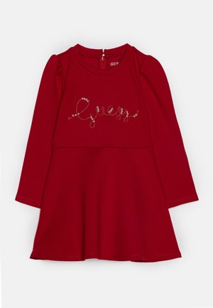 Robe rouge à manches longues pour enfant avec "Guess" écrit en cursive et décorée de petites perles sur la poitrine.