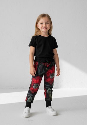 Czarna koszulka z krótkim rękawem zestawiona z czerwonymi dresami w kwiatowy wzór, wyposażonymi w pas z troczkiem i czarnymi mankietami na kostkach. Białe sneakersy.