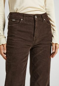 Bruine corduroy broek met verticale strepen, voorzien van een knoopsluiting, zijzakken en een iets relaxte pasvorm. De stof heeft een zachte textuur.