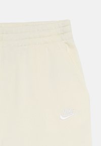 Off-white Nike hlače z elastičnim pasom, stranskim žepom in belim izvezenim Nike logom na sprednji desni strani.