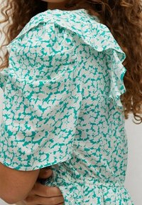 Vestido de estampado floral en turquesa y blanco, con mangas con volantes, una textura de tela suave y un detalle de cintura elástica.