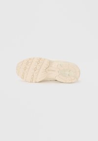 Semelle de sneaker beige clair avec un motif de caoutchouc texturé. Présente un bout arrondi et un soutien de la voûte plantaire avec un détail de logo près du talon.