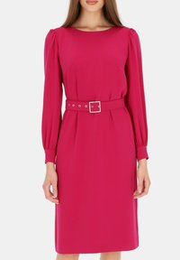 Fuksjowa sukienka z długimi rękawami, okrągłym dekoltem i paskiem w talii z prostokątną srebrną klamrą i dekoracyjnymi ćwiekami. Gładka tekstura.