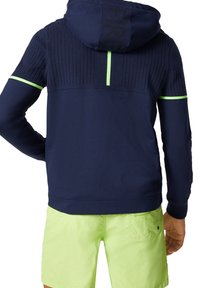 Hoodie bleu marine avec texture côtelée, accents vert fluo sur les poignets et le dos. Comprend une capuche avec cordon de serrage et un détail de logo.
