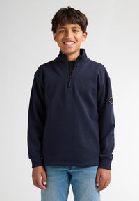 Felpa pullover blu navy con colletto alto e zip parziale. Presenta maniche lunghe e una toppa rotonda sulla manica sinistra. Texture del tessuto morbida.
