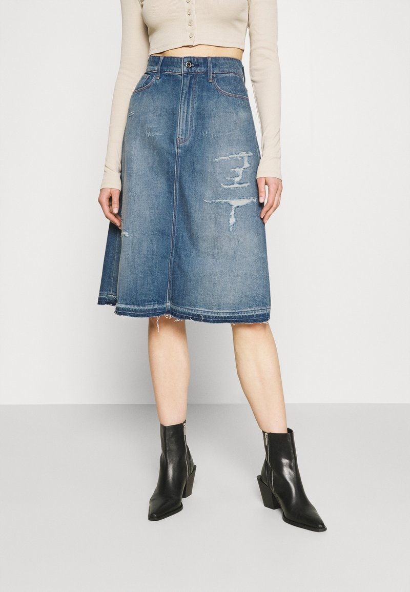 Jeans A-linje kjol i medelblå med slitna detaljer. Har hög midja, framknäppning med knappar och rå nederkant. Stylar med svarta ankelstövlar.