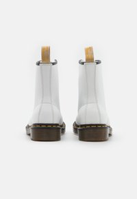 Botas de tobillo de cuero blanco con tirador amarillo, lados elásticos negros y costuras amarillas contrastantes en una suela de goma gruesa.