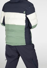 Puffer jacket in navy, green, and white stripes; features a hood, zip pockets, and quilted texture; logo displayed on the back.