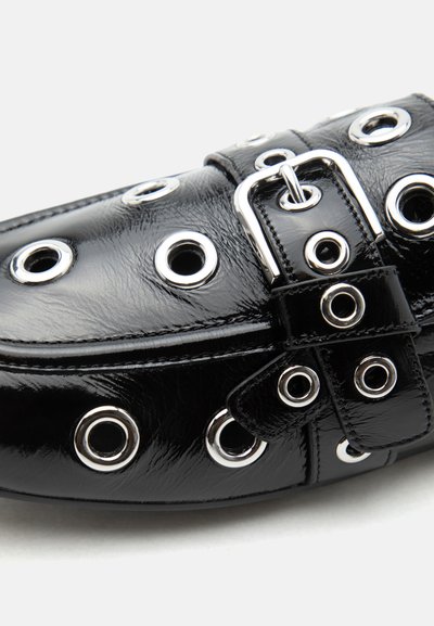 Μαύρο παπούτσι loafer από δέρμα με γυαλιστερό φινίρισμα, με ασημένιες τρύπες για κορδόνια και μια μεγάλη ασημένια αγκράφα στην κορυφή, εμφανίζεται σε κοντινή λήψη σε λευκό φόντο.