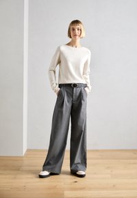 Light beige long-sleeve sweater paired with high-waisted, wide-leg gray trousers and white shoes with black soles. The outfit is simple and tailored.