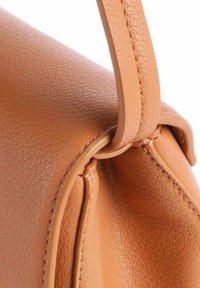 Leren handtas van lichtbruin leer, close-up, met een gestructureerd oppervlak, een gebogen vorm en een gedetailleerde riembevestiging met zichtbare stiksels.