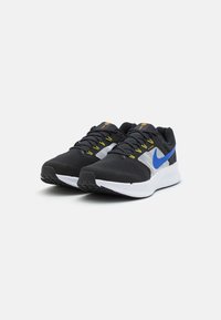 Chaussures de sport noires avec empeigne en mesh, accents gris et bleus, lacets jaunes, et semelle extérieure blanche. Présentent un design texturé et un logo détaillé.